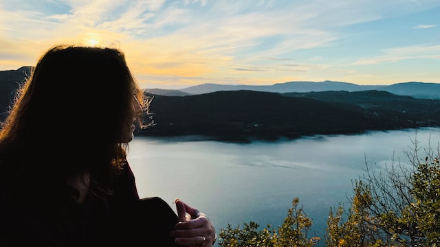 Image of person on cliff overlooking water and mountains